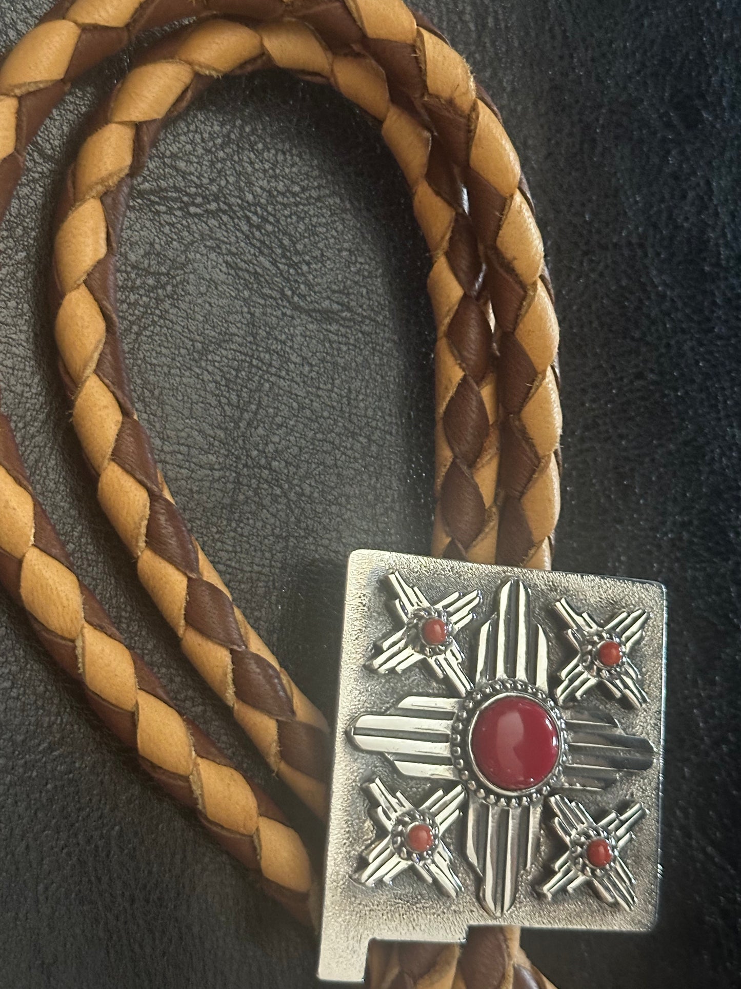 Close-up view of sterling silver Zia symbol bolo tie with 13mm Rosarita stone, red coral, and handmade elk skin braid